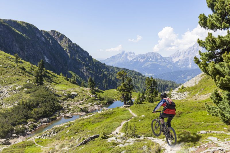 Mountainbiker on fast downhill driving on mountain Reiteralm to Lake Spiegelsee with mountain Dachstein in the background